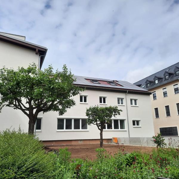 Mai 2026: Hinter dem Haus ist die Anlage eines kleinen Gartens vorbereitet, die gro&szlig;en Fenster im EG geh&ouml;ren zum Refektorium (Speiseraum) und Verwaltungsb&uuml;ro 